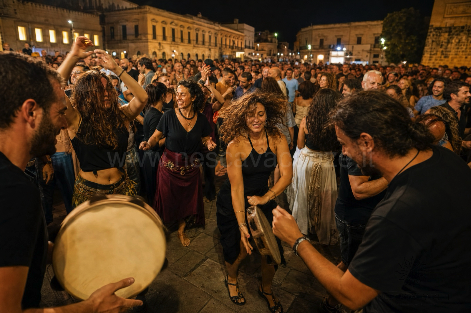 Folla che balla la pizzica di notte in piazza durante una serata di musica popolare salentina