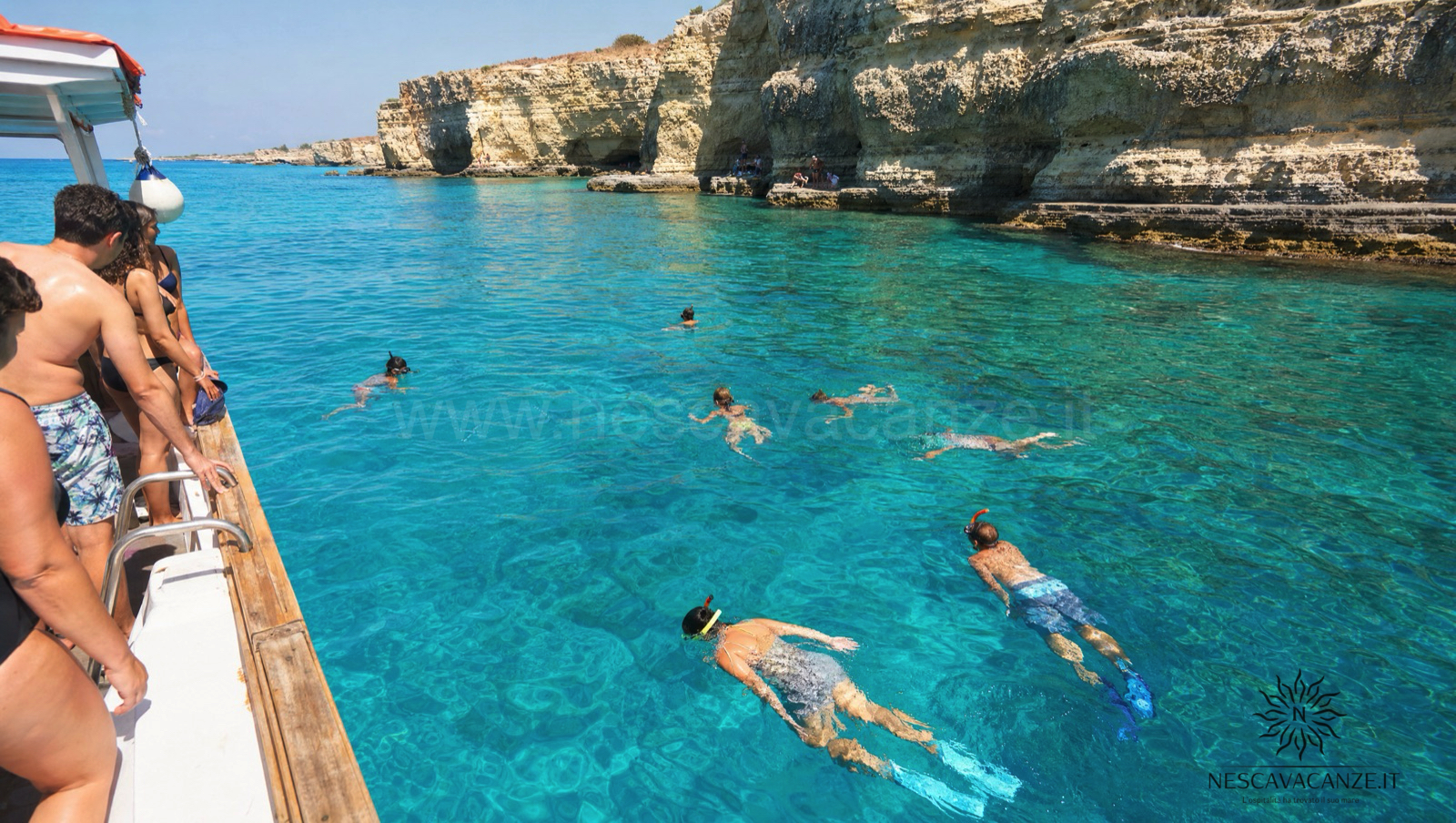 Persone che nuotano e fanno snorkeling nell'acqua turchese e trasparente accanto alla barca durante una sosta bagno lungo la costa del Salento