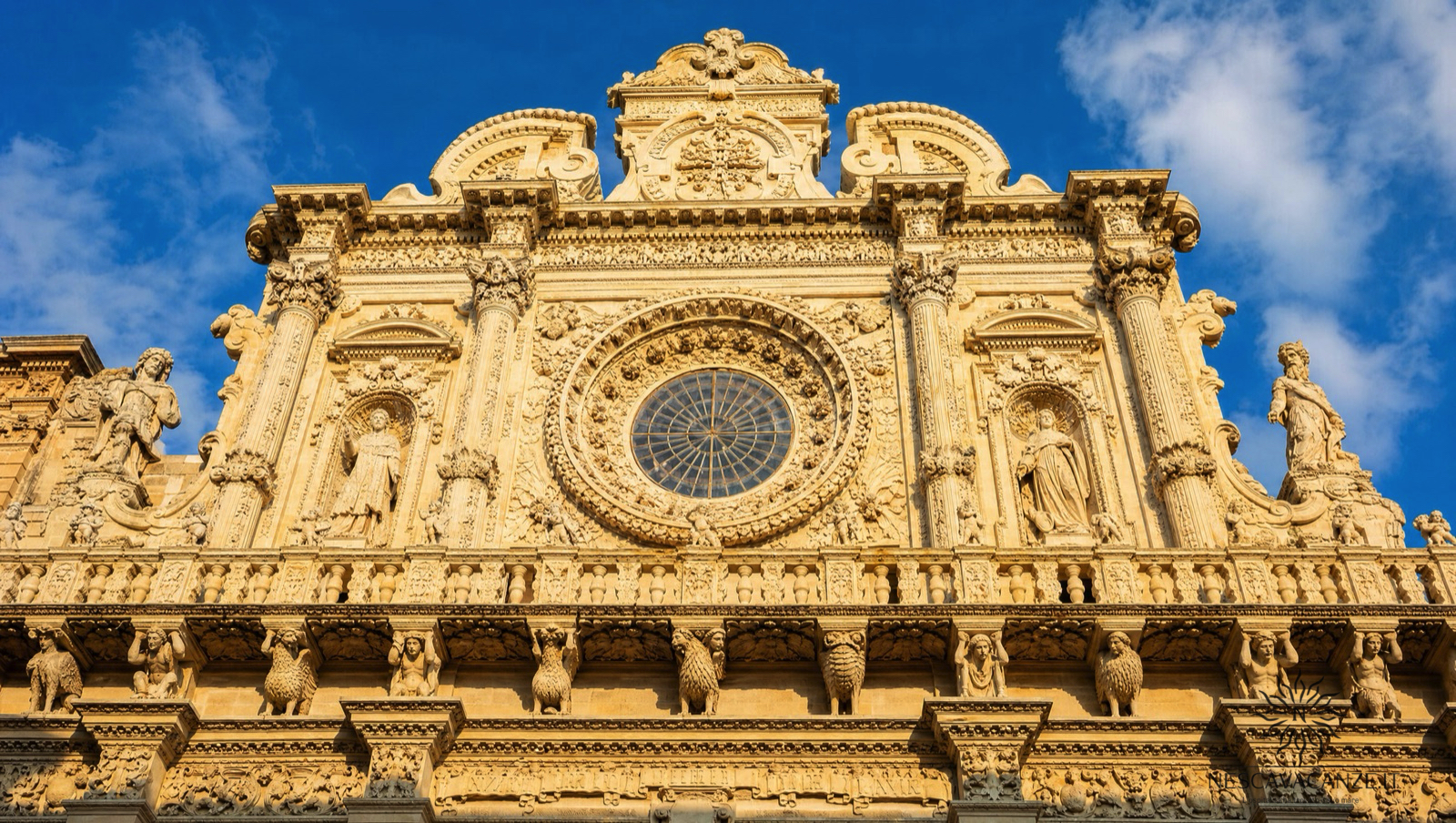 La facciata barocca riccamente scolpita della Basilica di Santa Croce a Lecce in pietra dorata, con il rosone e le statue, illuminata dal sole