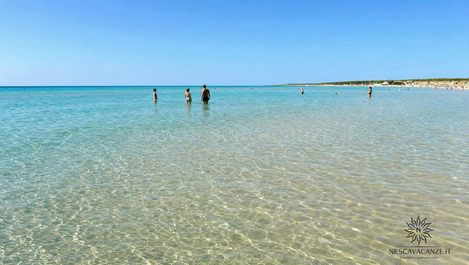 I fondali bassi e trasparenti di Pescoluse con persone che camminano nell'acqua turchese lontano dalla riva, sopra la sabbia chiara